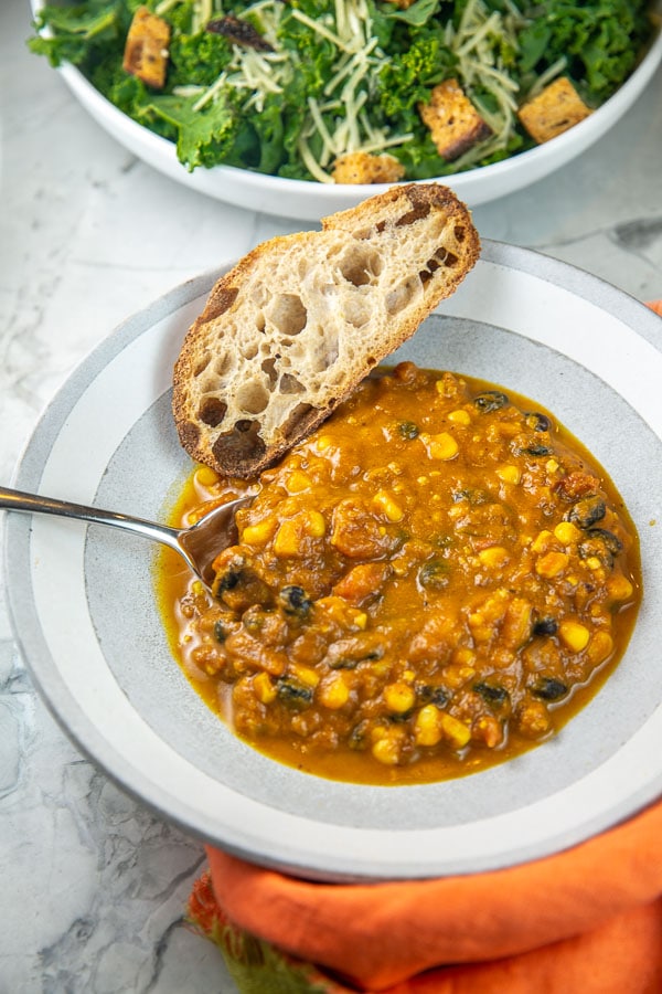 bowl of soup with a spoon in it and a slice of bread resting on the side.