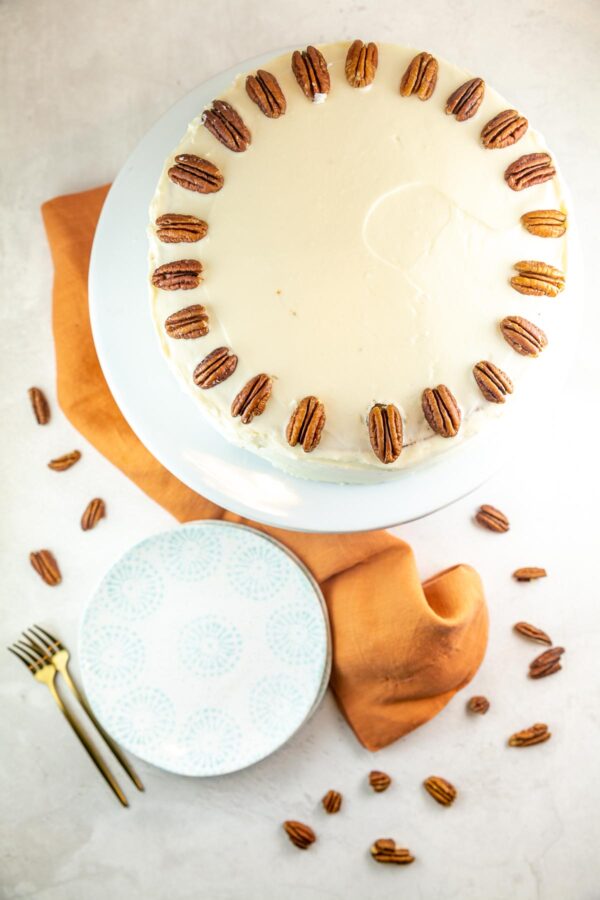 cake decorated with smooth cream cheese frosting and halved pecans