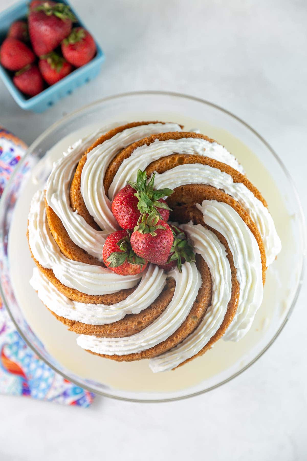 overhead view of tres leches bundt cake with whipped cream stripes and fresh strawberries