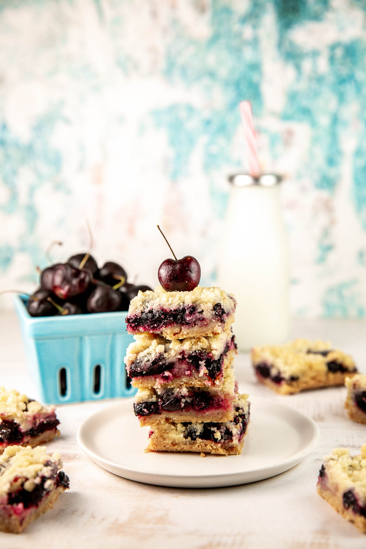 cherry pie bars on a plate with a basket of fresh cherries and a glass of milk