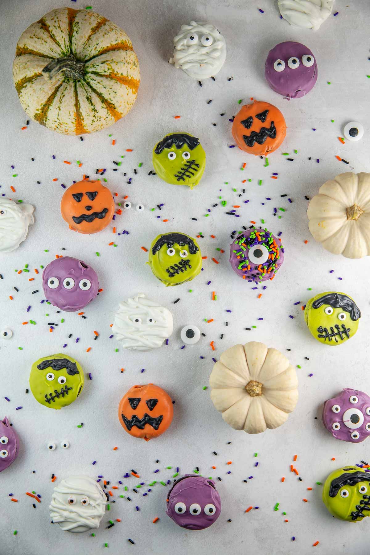 oreos dipped in chocolate and decorated for Halloween with sprinkles and pumpkins in the background.