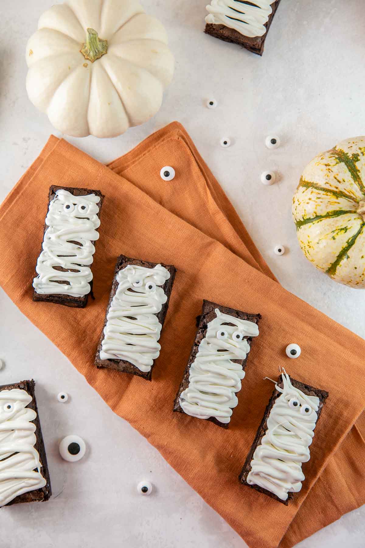 four mummy brownies on an orange cloth napkin.