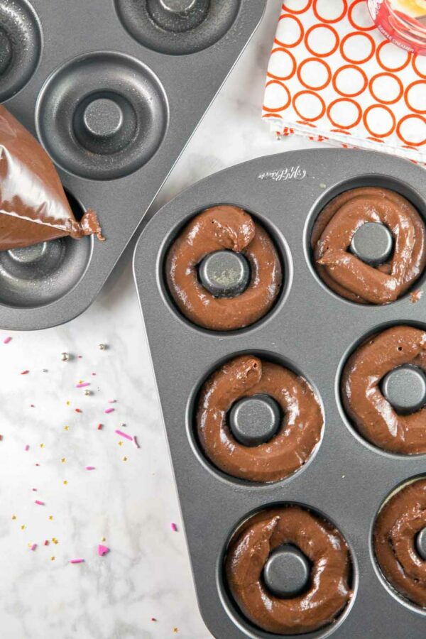 chocolate cake donut batter being piped into a donut pan