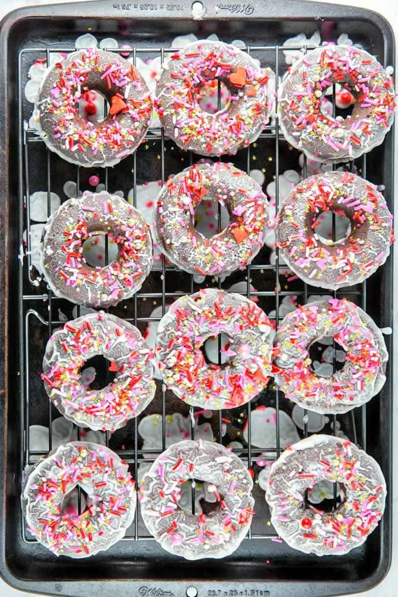 12 chocolate cake donuts dripping glaze on a sheet pan.