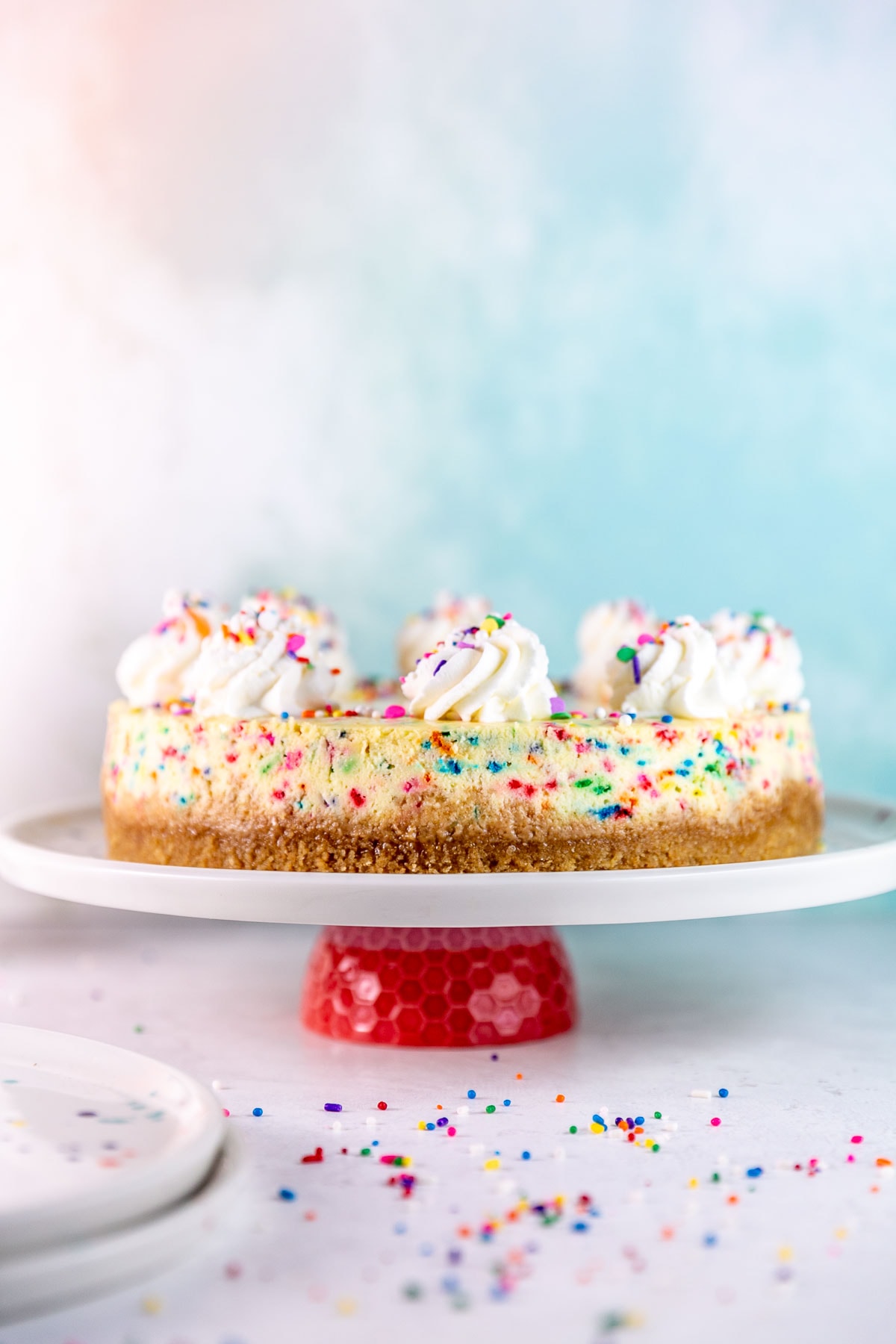 side view of a sprinkle filled funfetti cheesecake with whipped cream swirls on top
