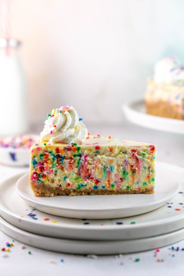 slice of creamy cheesecake filled with brightly colored sprinkles and whipped cream on top