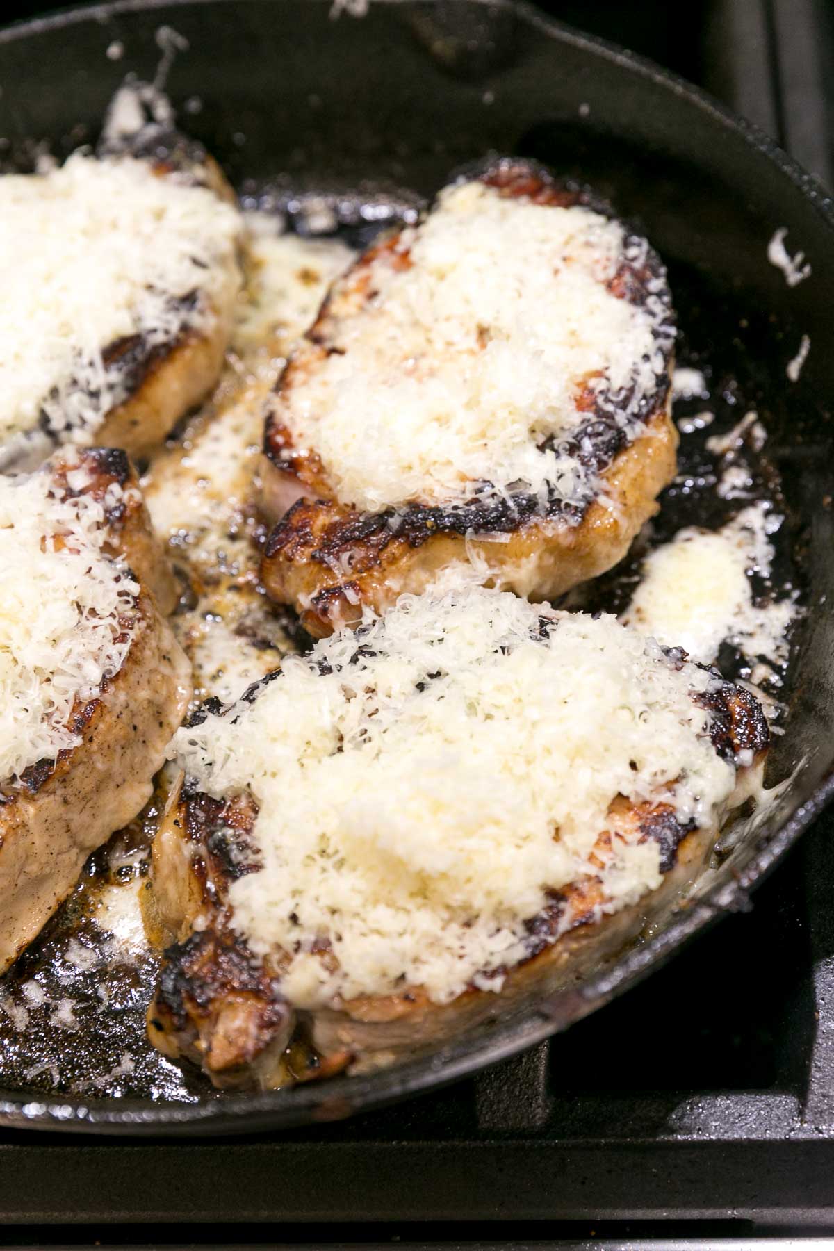 seared pork chops in a cast iron skillet covered with shredded cheese just starting to melt