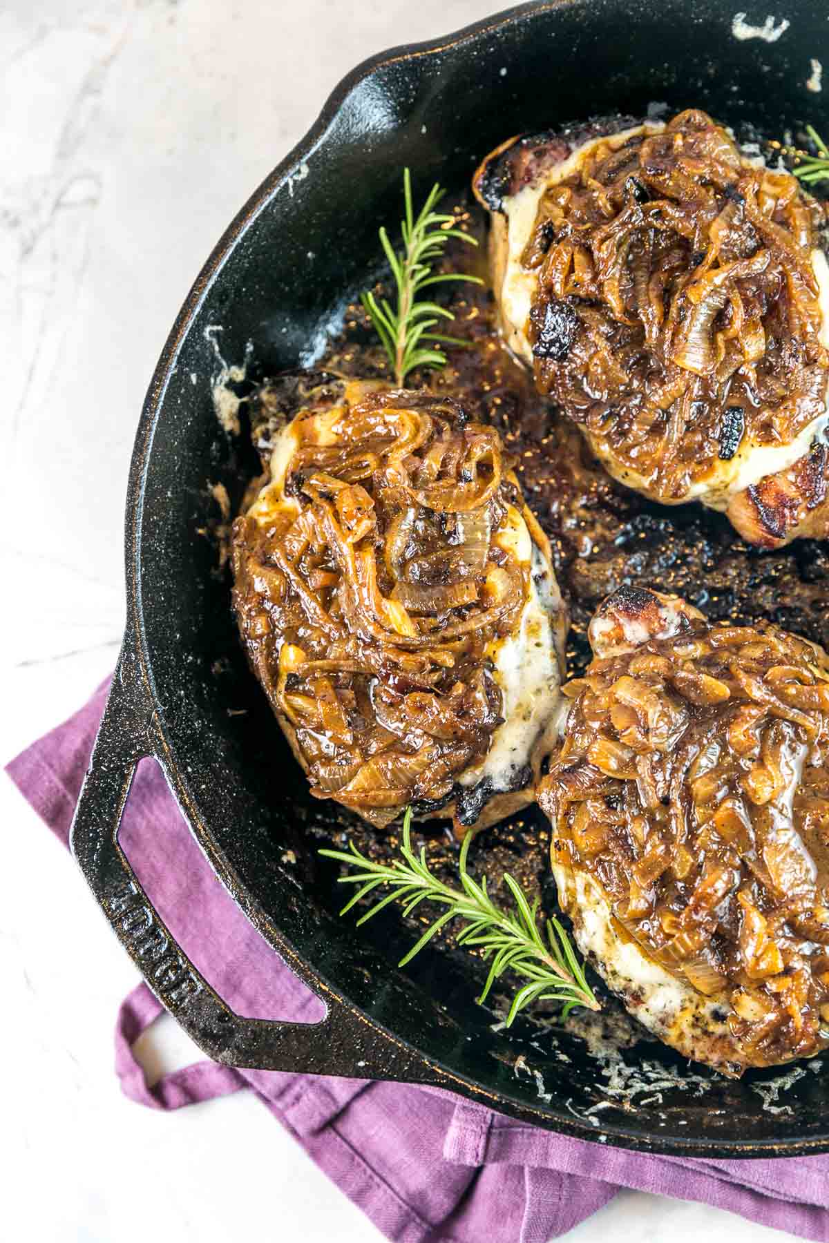 pork chops smothered with melted cheese and caramelized onions in a cast iron skillet
