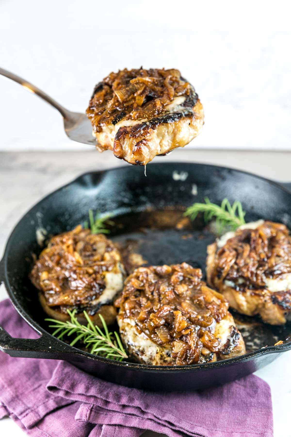 metal spatula lifting one french onion pork chop out of a cast iron skillet