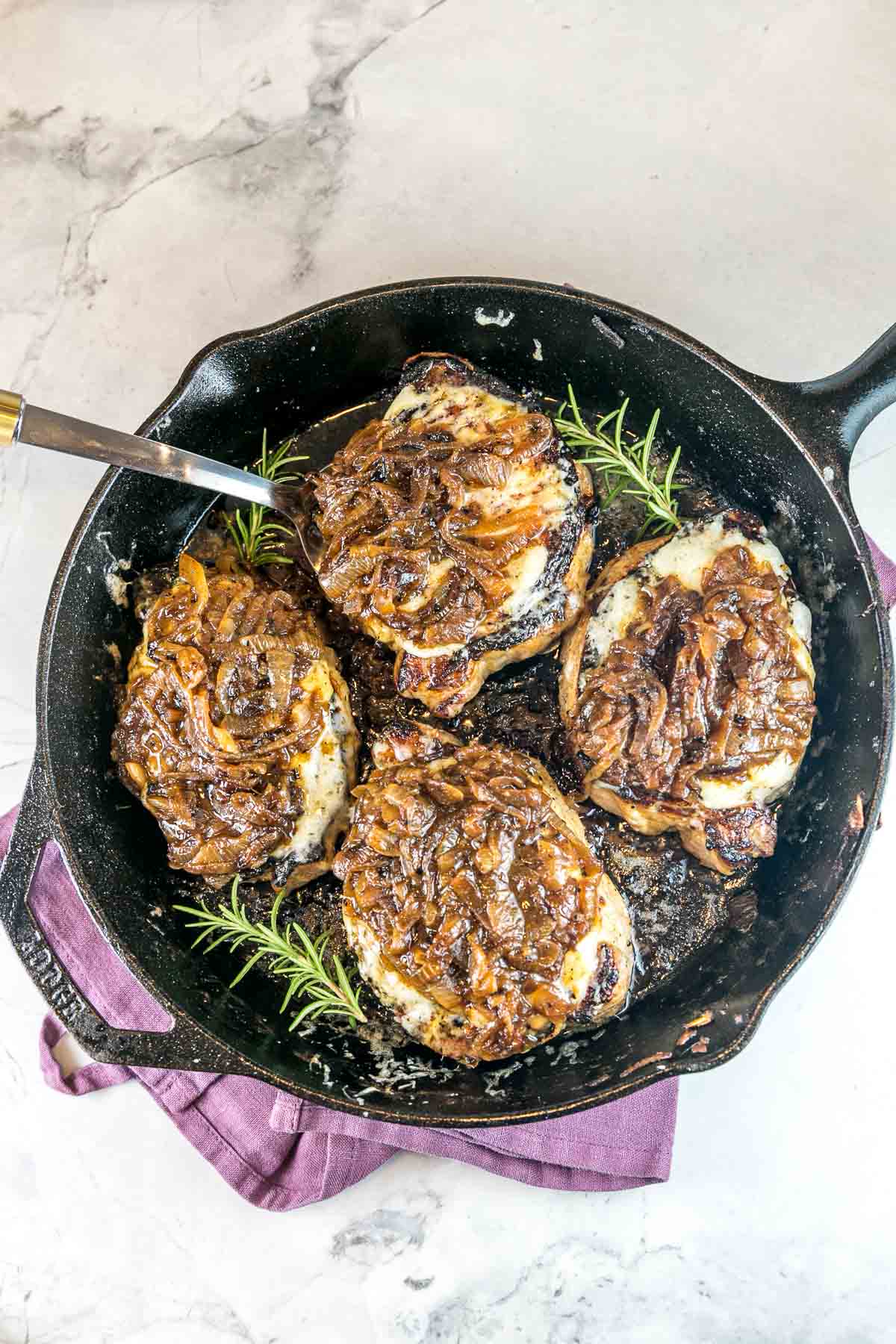 four pork chops in a cast iron skillet smothered with onions and cheese