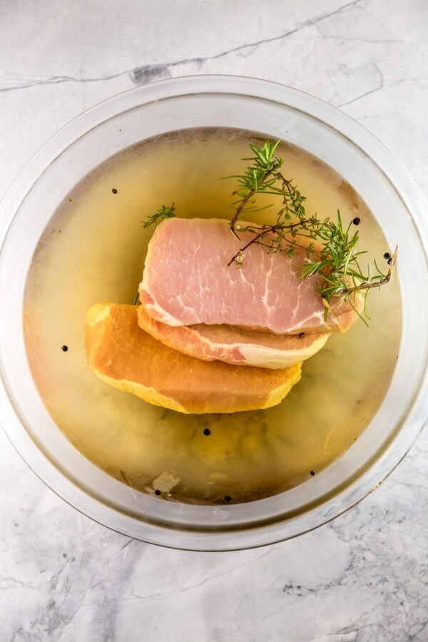 four thick pork chops in a bowl filled with brining solution