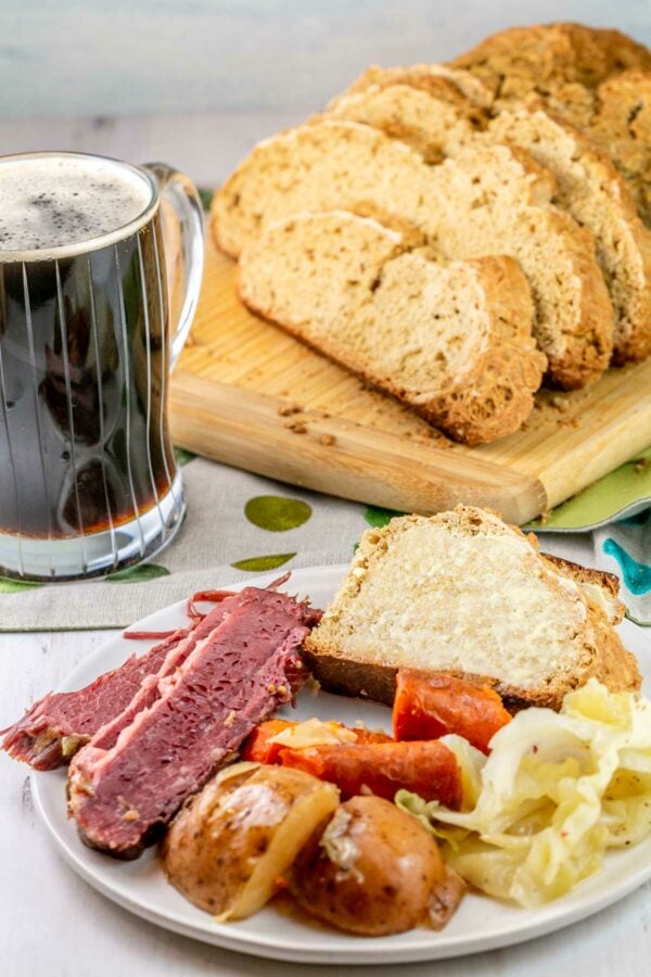 soda bread on a plate with corned beef, cabbage, and potatoes with beer in the background