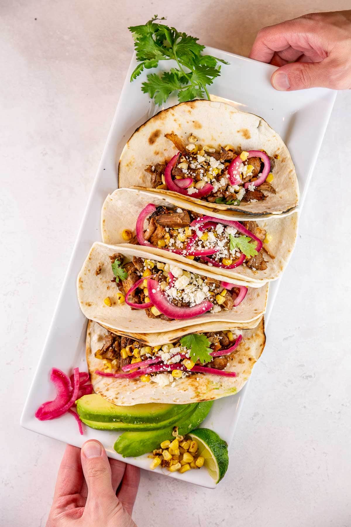 carnitas tacos on a white serving plate with extra avocado and limes