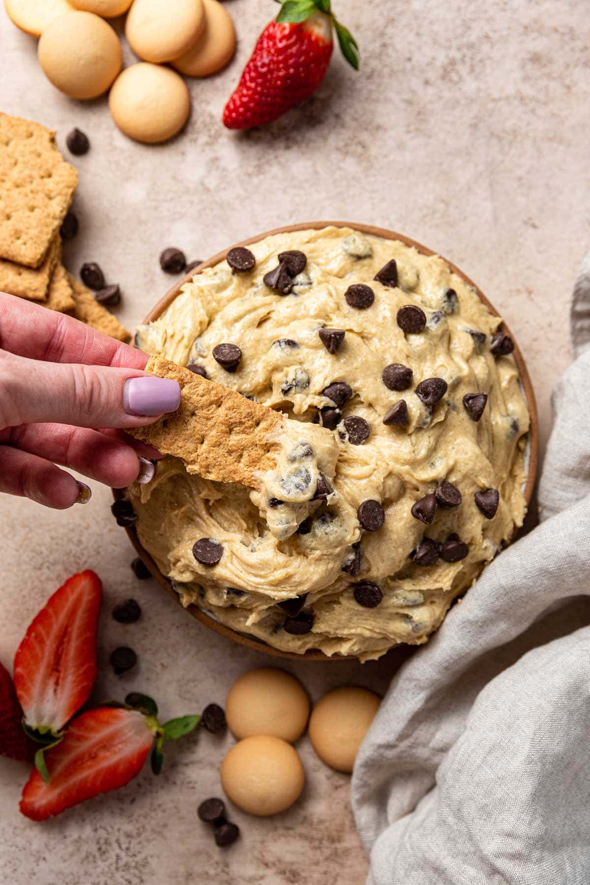hand holding a graham cracker scooping up cookie dough dip out of a bowl
