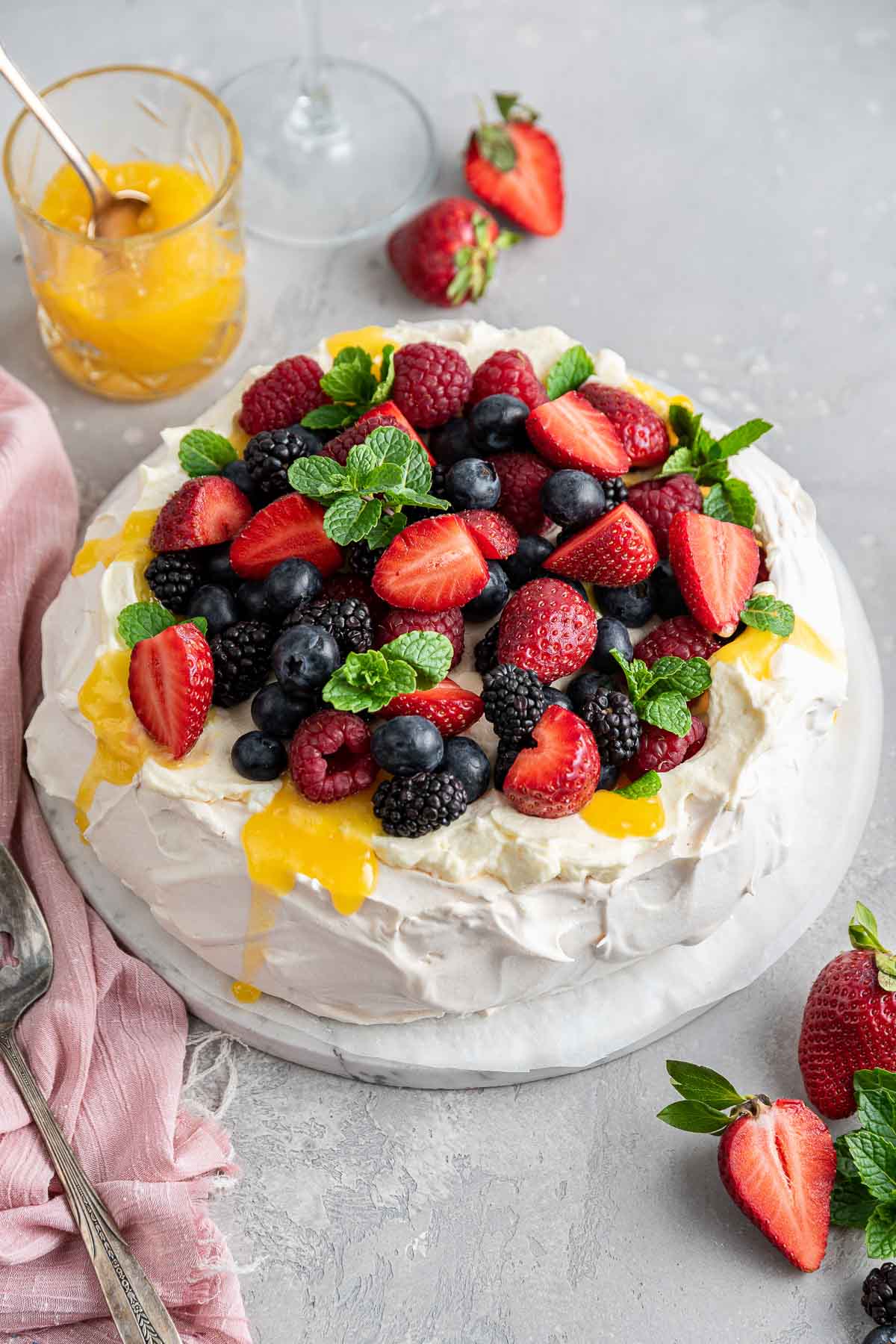 fluffy white pavlova topped with a big pile of fresh berries and lemon curd