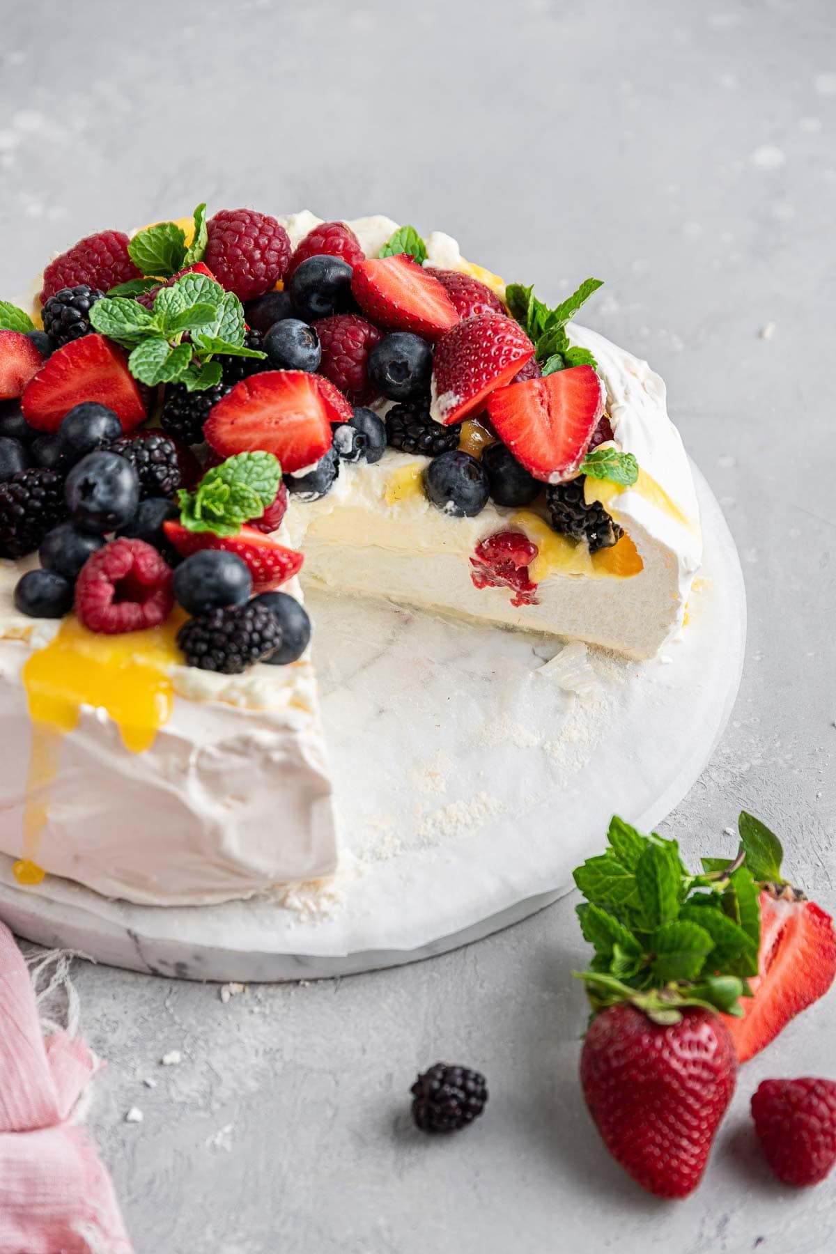 pavlova topped with fresh berries and lemon curd with one slice removed