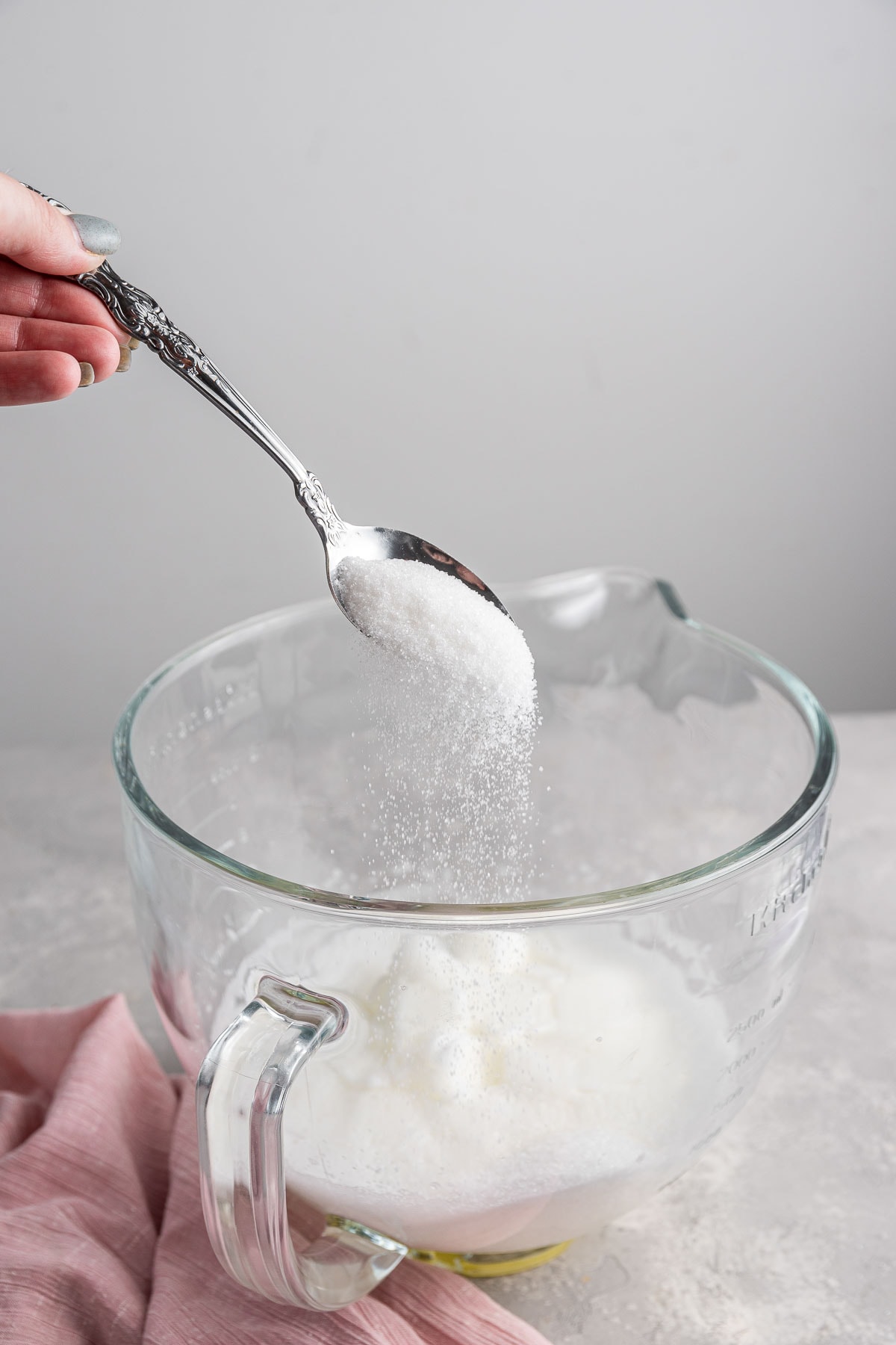 spooning sugar into a bowl of whipped egg whites