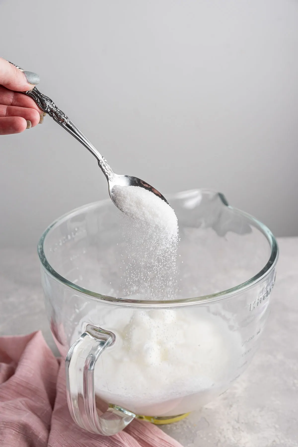 spooning sugar into a bowl of whipped egg whites