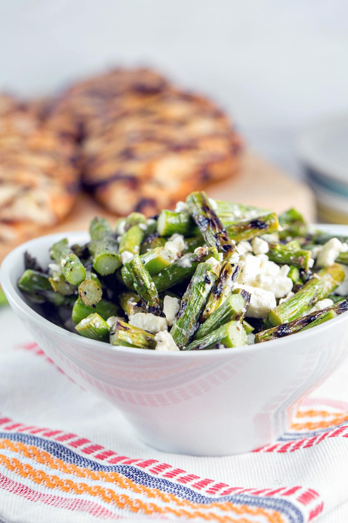 white bowl filled with grilled asparagus salad in front of grilled chicken