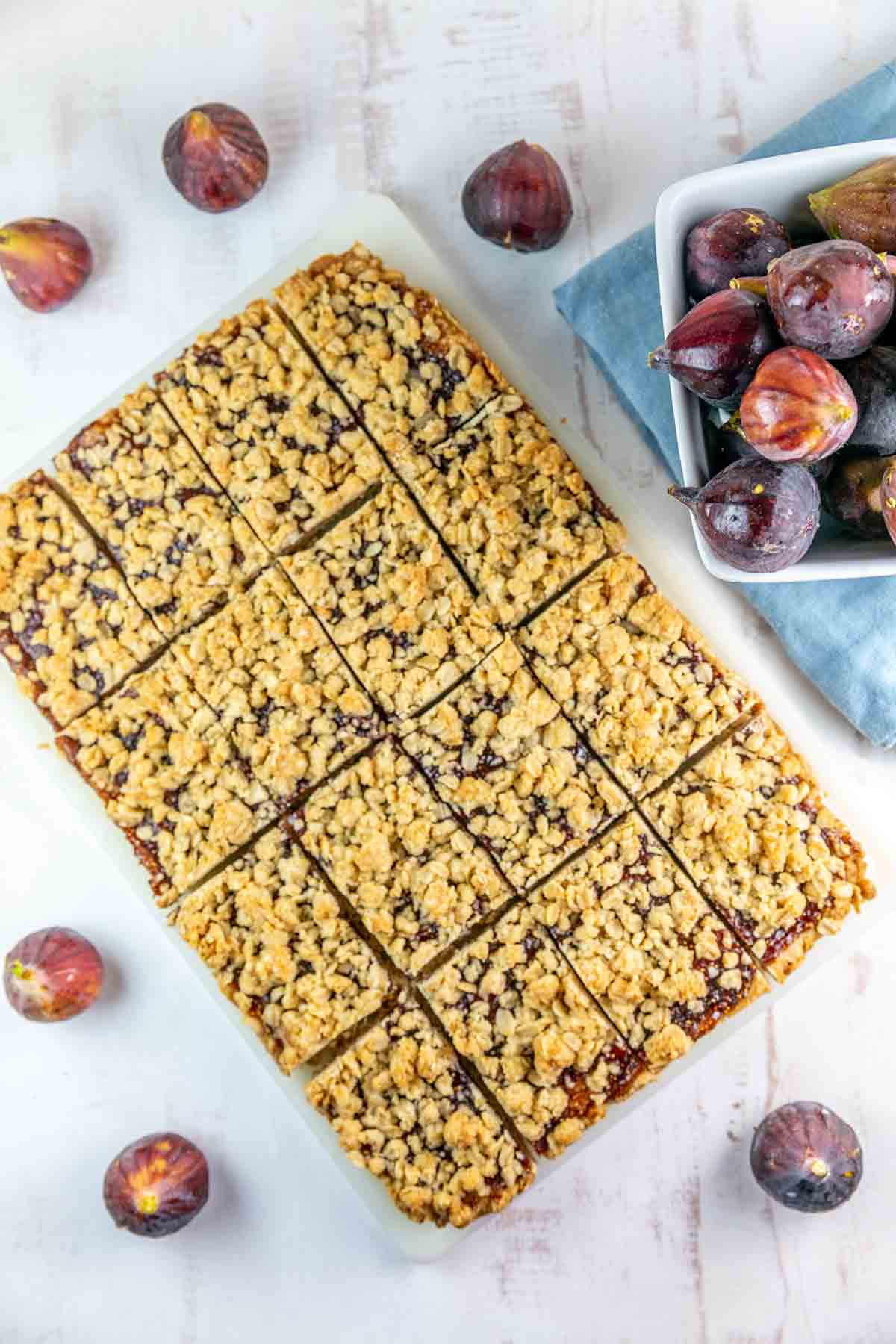Fig bars cut into squares with a white background and fresh figs next to them. 