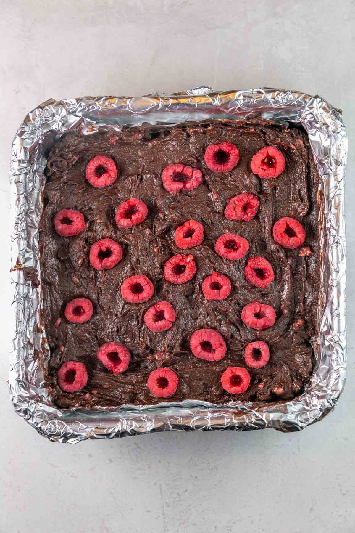 Brownie batter in pan topped with raspberries. 