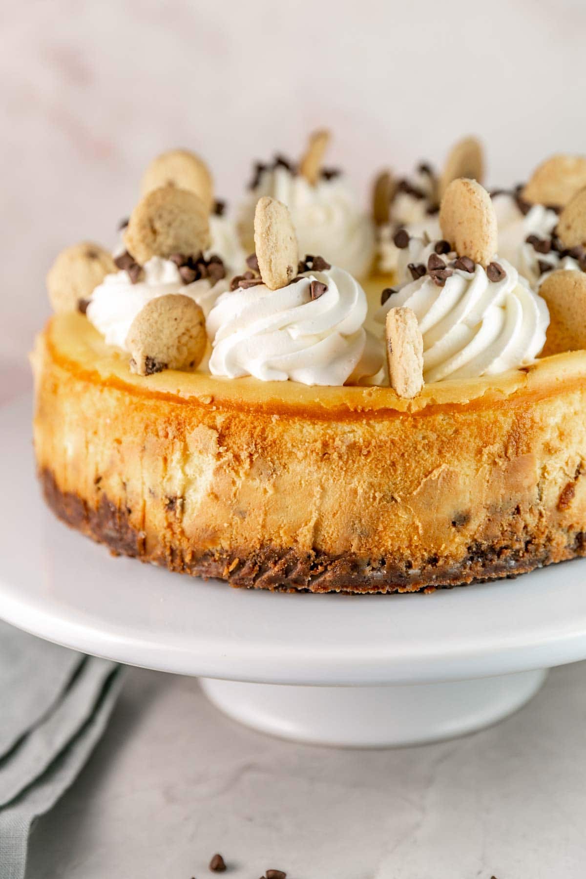 Cheesecake on a white cake stand topped with whipped cream and mini cookies.