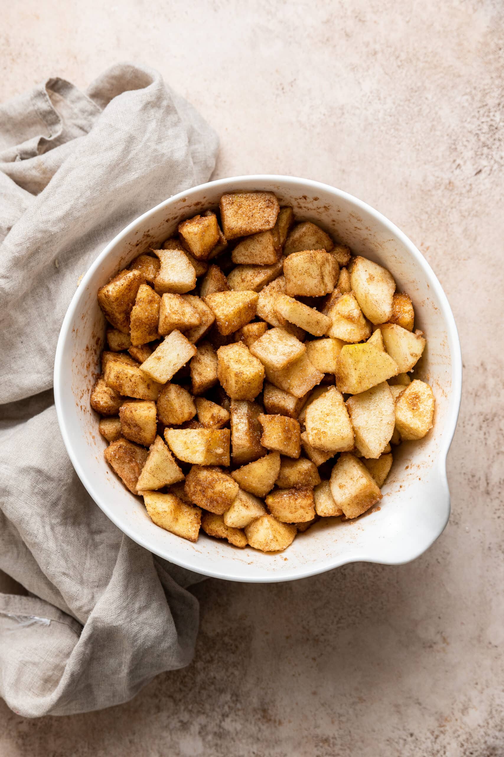 mixing bowl full of apple chunks mixed with cinnamon and sugar