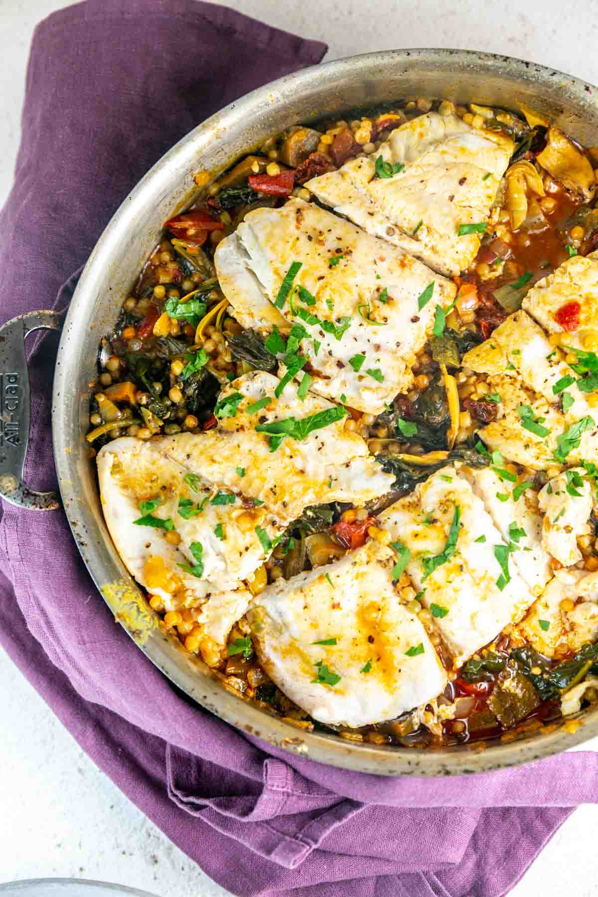 Top view of fish in a silver pot with couscous and sauce underneath. 