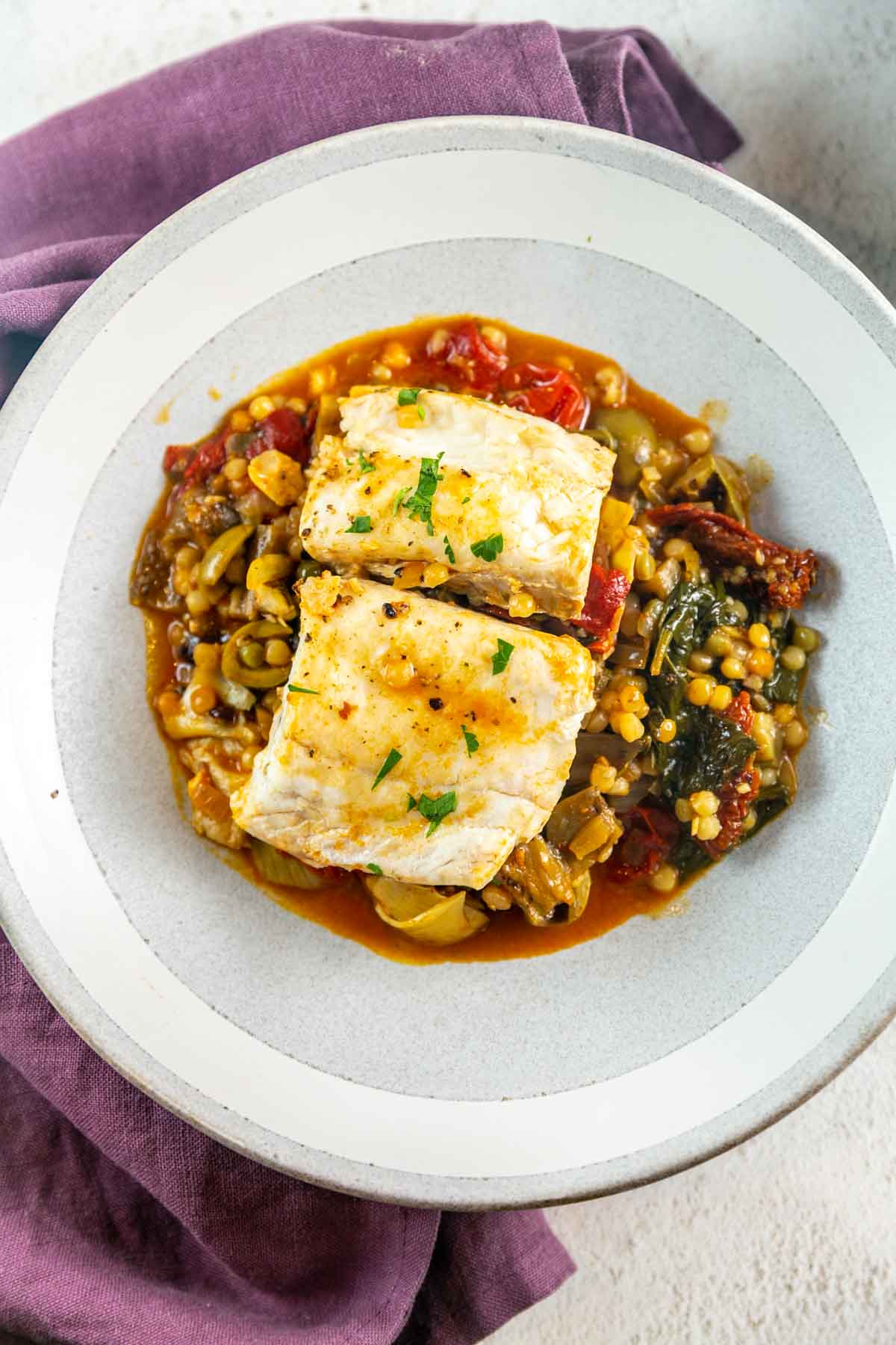 Top view of white fish with red vegetables sauce in a grey bowl.