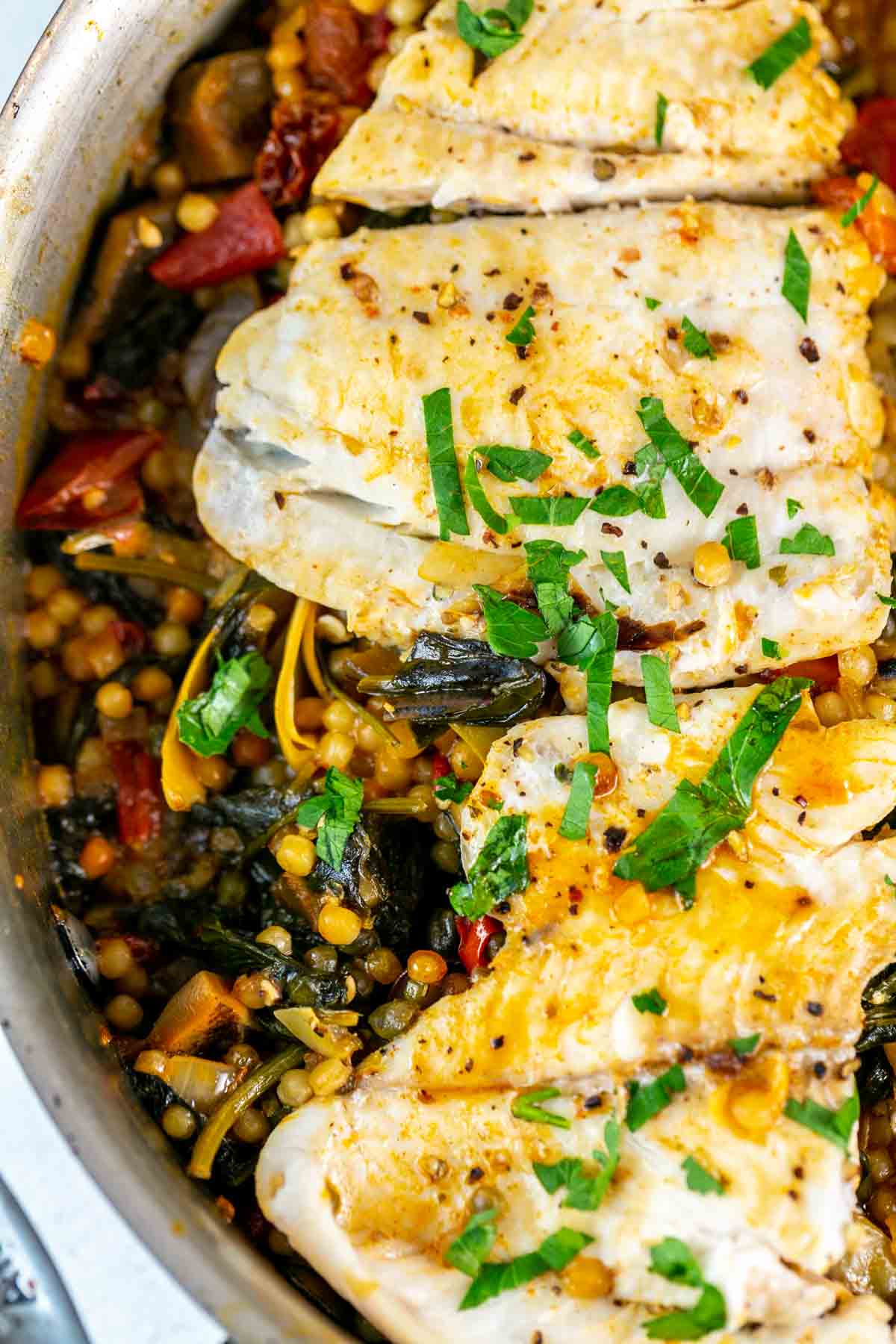 Close up of white fish with couscous and vegetables in a silver pan.