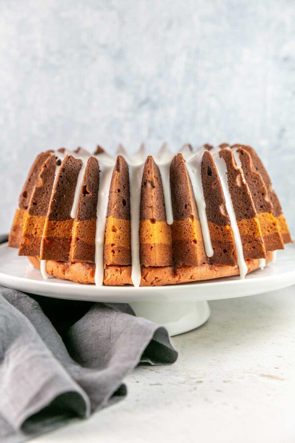 Bundt cake with dripping glaze on top on a white cake stand. 