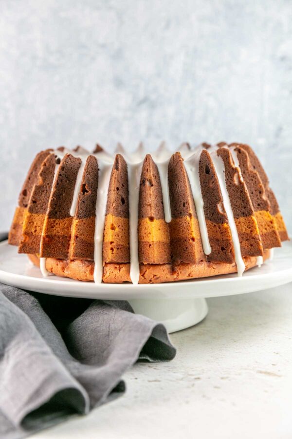 Bundt cake with dripping glaze on top on a white cake stand.