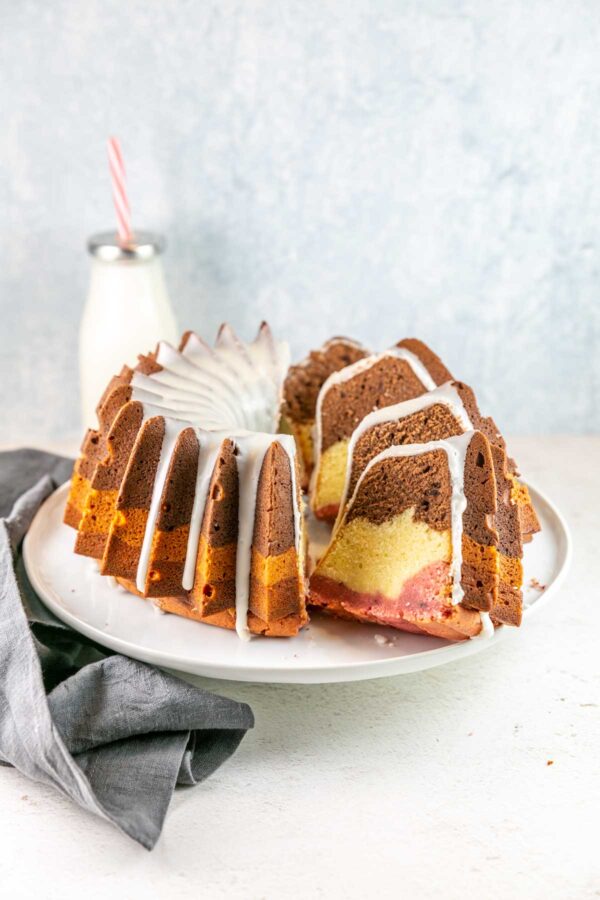 Neapolitan bundt cake on a white cake stand with half of the cake in separated slices.