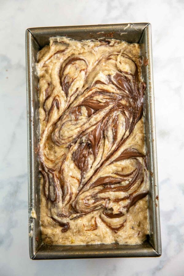 Top view of unbaked bread dough in a loaf pan with swirls of Nutella. 