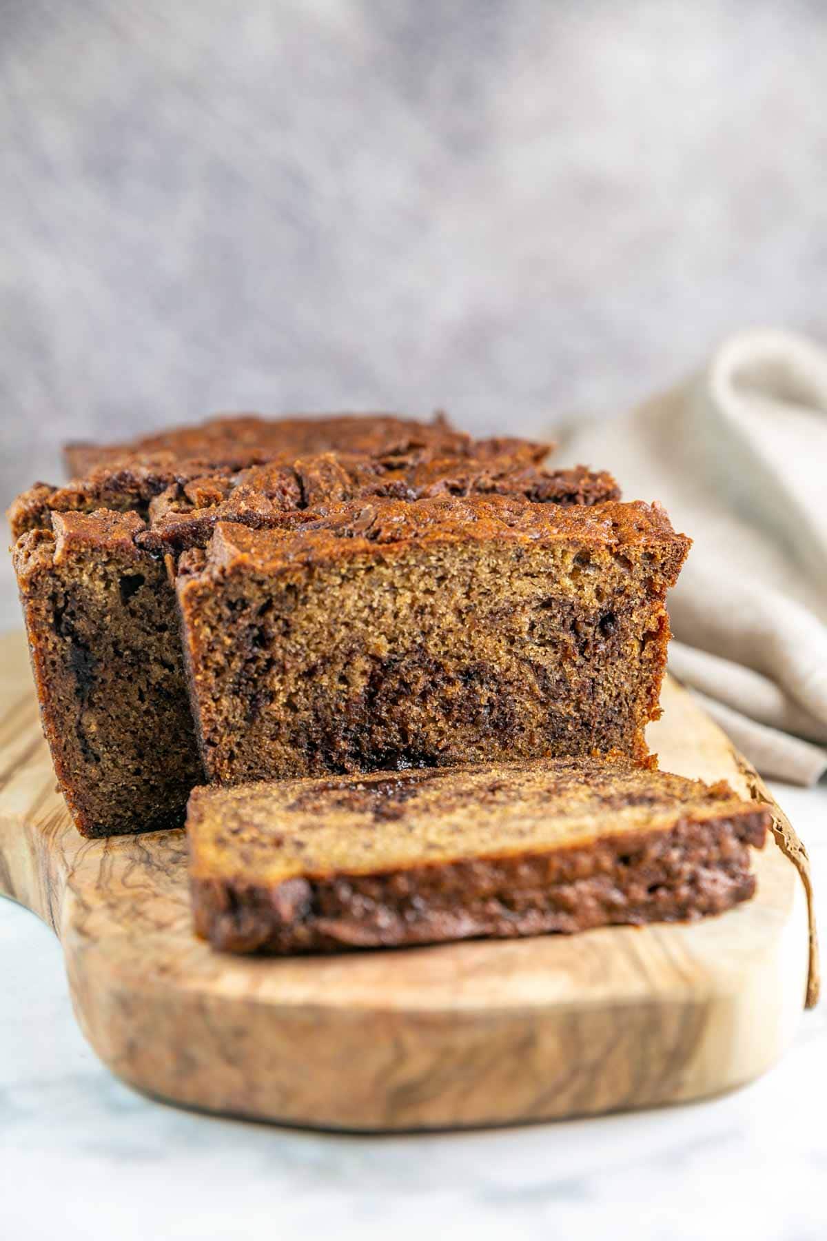 Sliced banana bread with swirls of chocolate on the inside on a wooden cutting board.