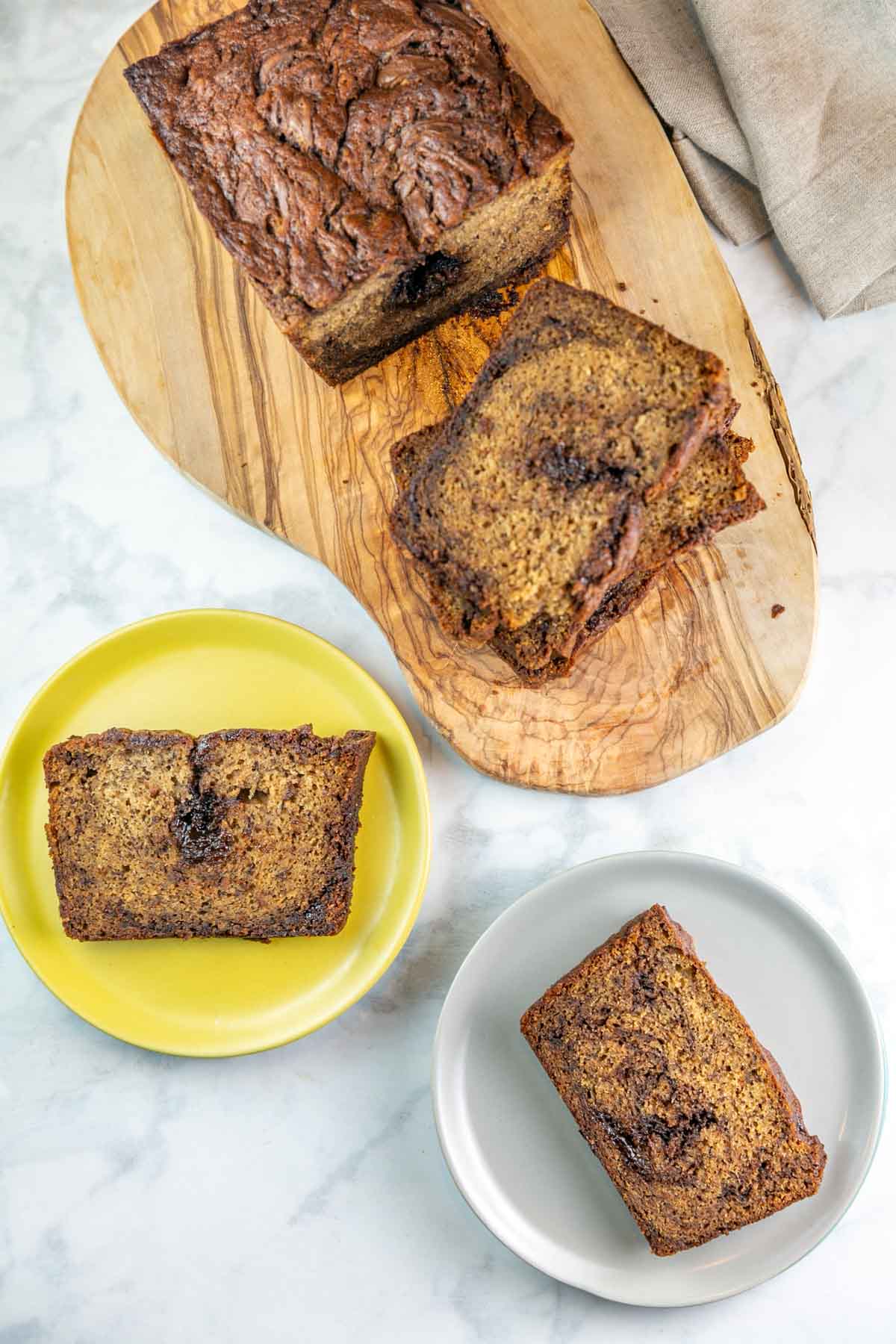 Top view of two plates with slices of banana bread on them and the rest of the loaf on a wooden cutting board.