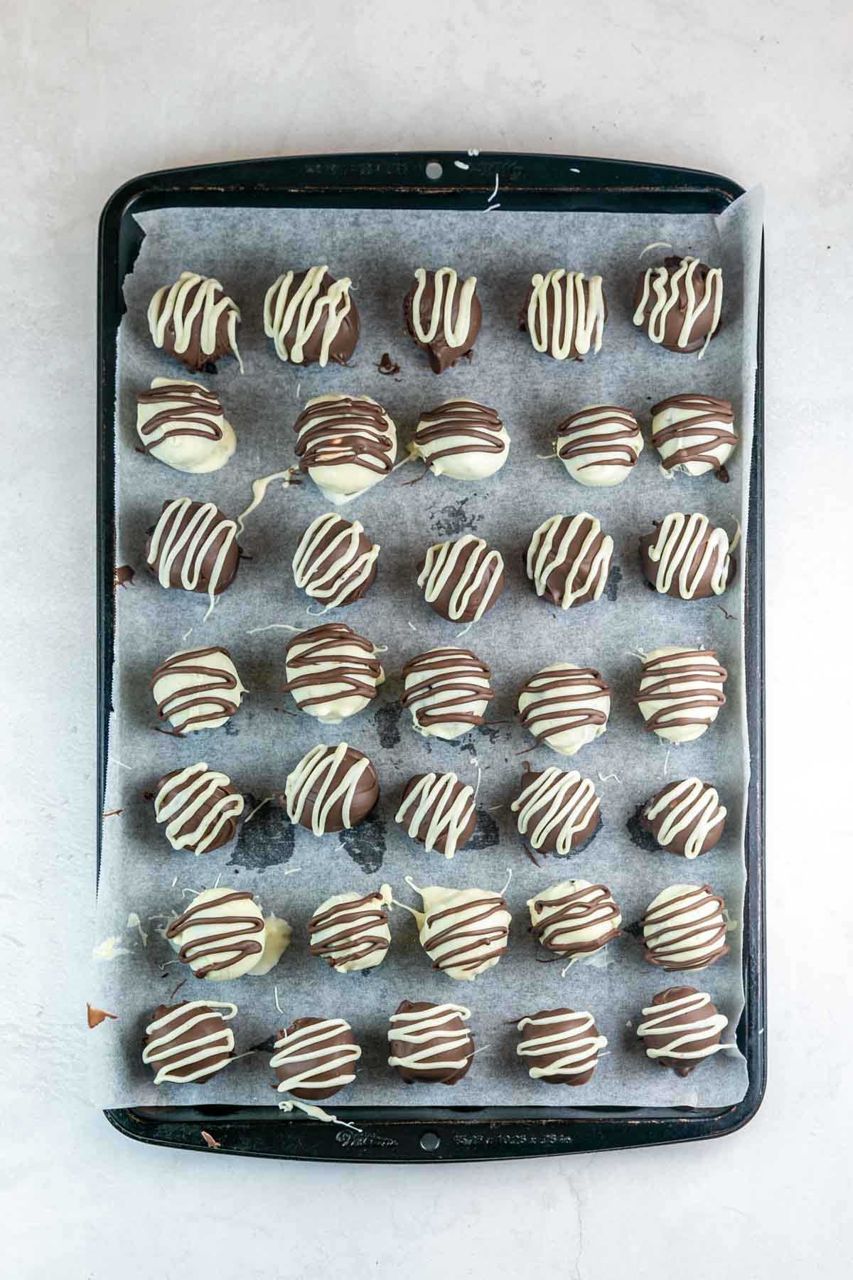 oreo truffles dipped in chocolate and drizzled with white chocolate on a cookie sheet