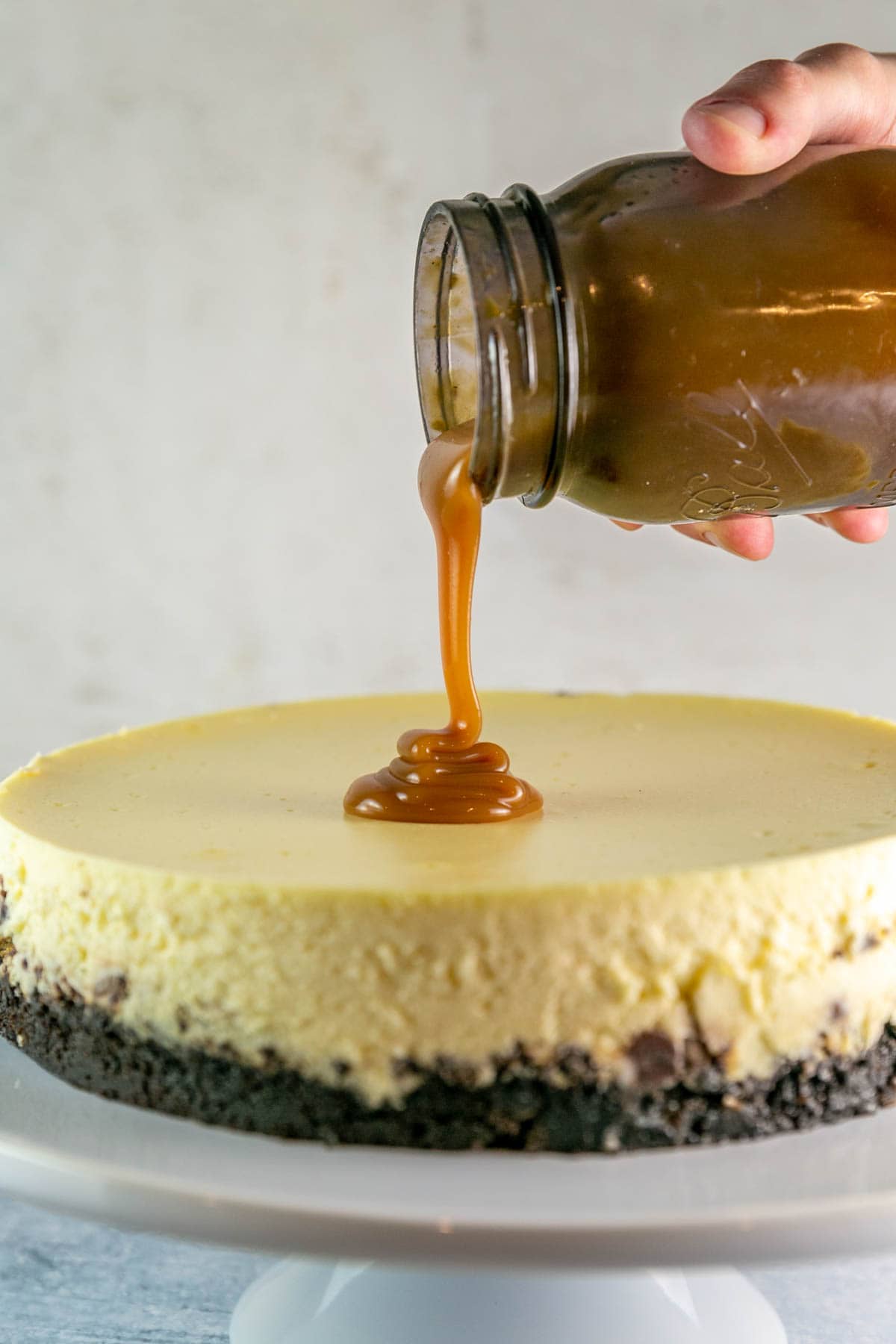 Cheesecake on a cake stand with caramel sauce being poured on top.