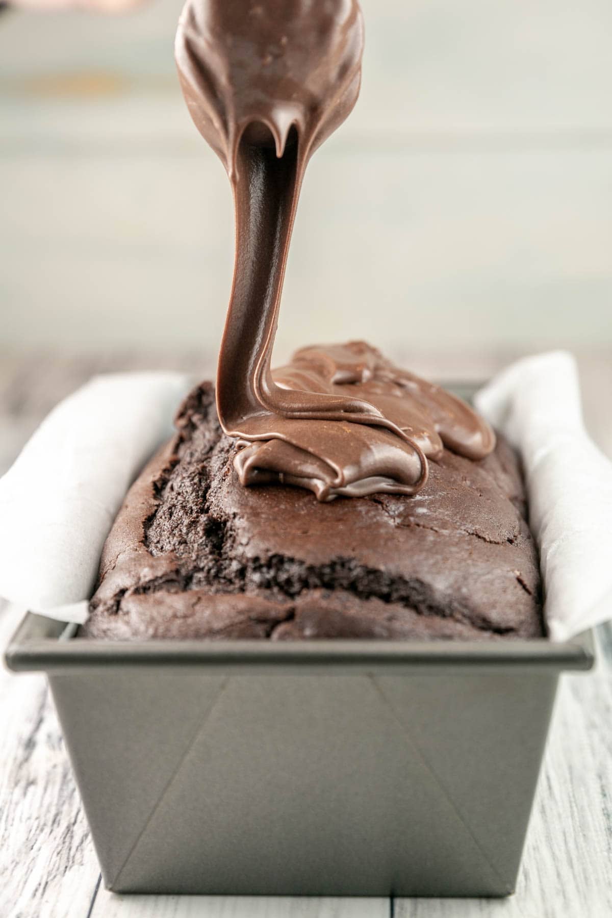 thick chocolate glaze being poured on a chocolate loaf cake