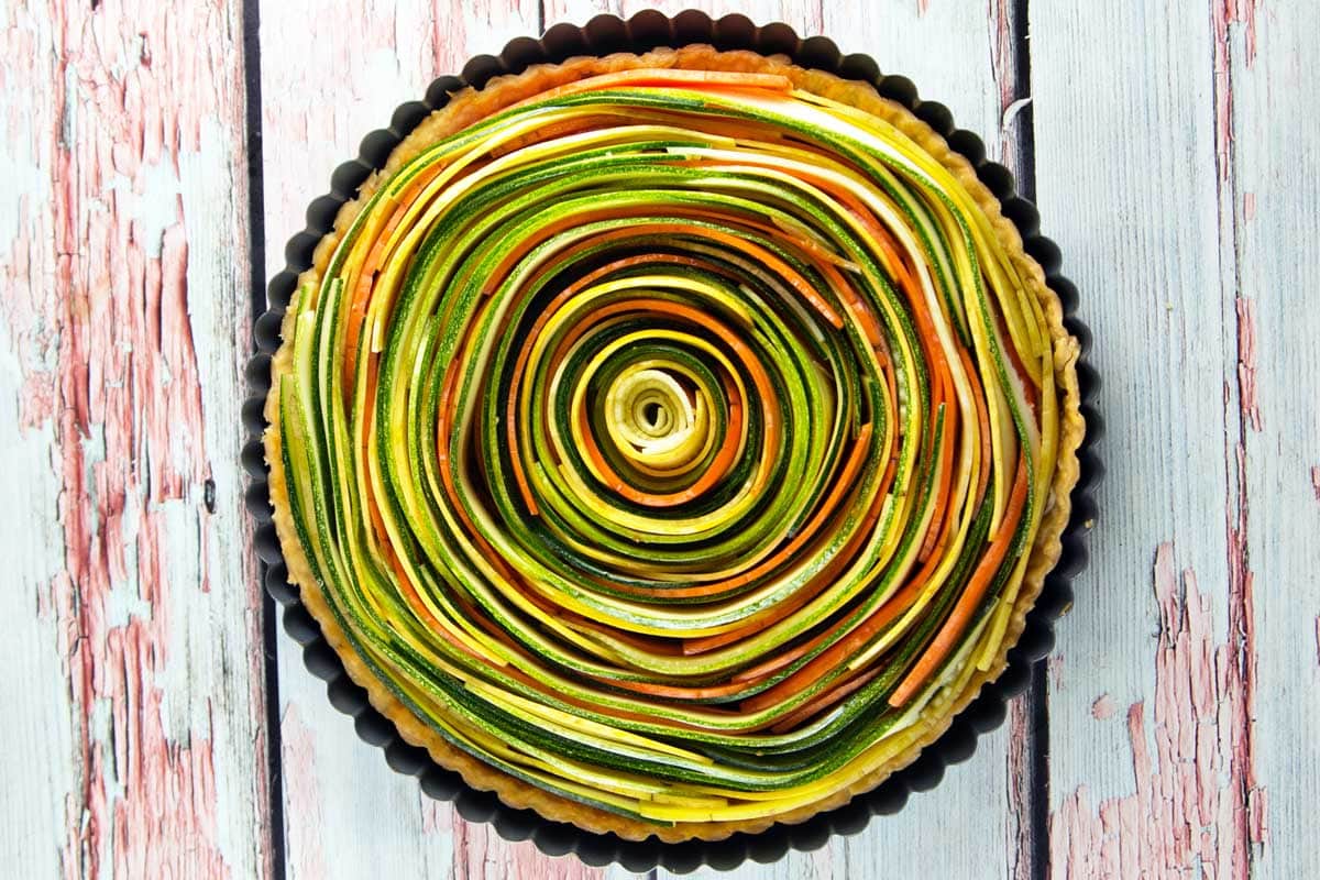 a spiral vegetable tart with concentric circles of zucchini, squash, and carrots in a tart pan