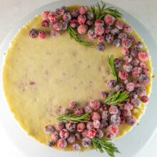 white chocolate cranberry cheesecake decorated with sugared cranberries and rosemary sprigs