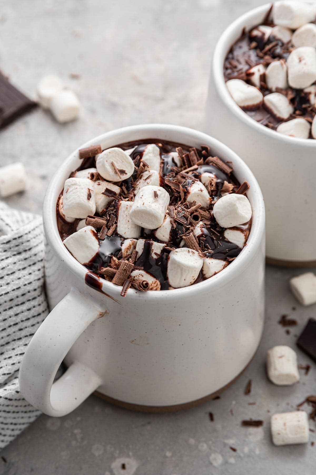 two mugs full of hot chocolate topped with marshmallows and chocolate shavings.