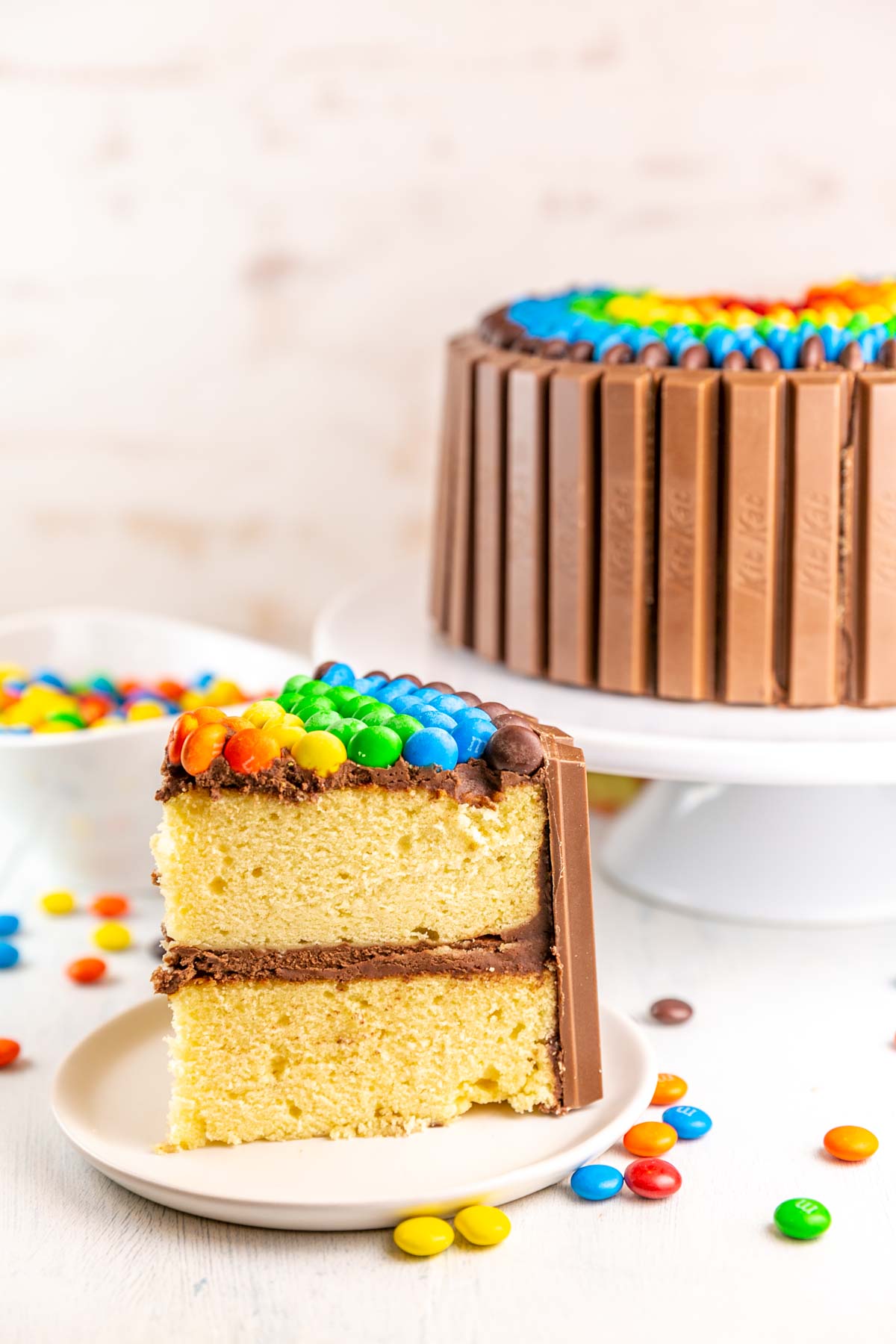 Slice of cake with candy cake in the background on a white cake stand. 