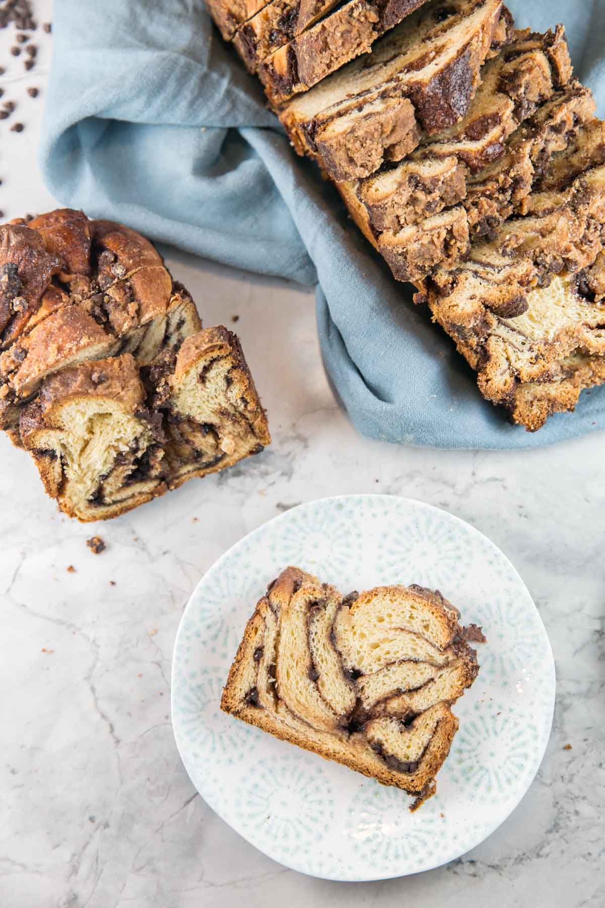 one slice of chocolate babka on a blue and white plate next half an uncut loaf