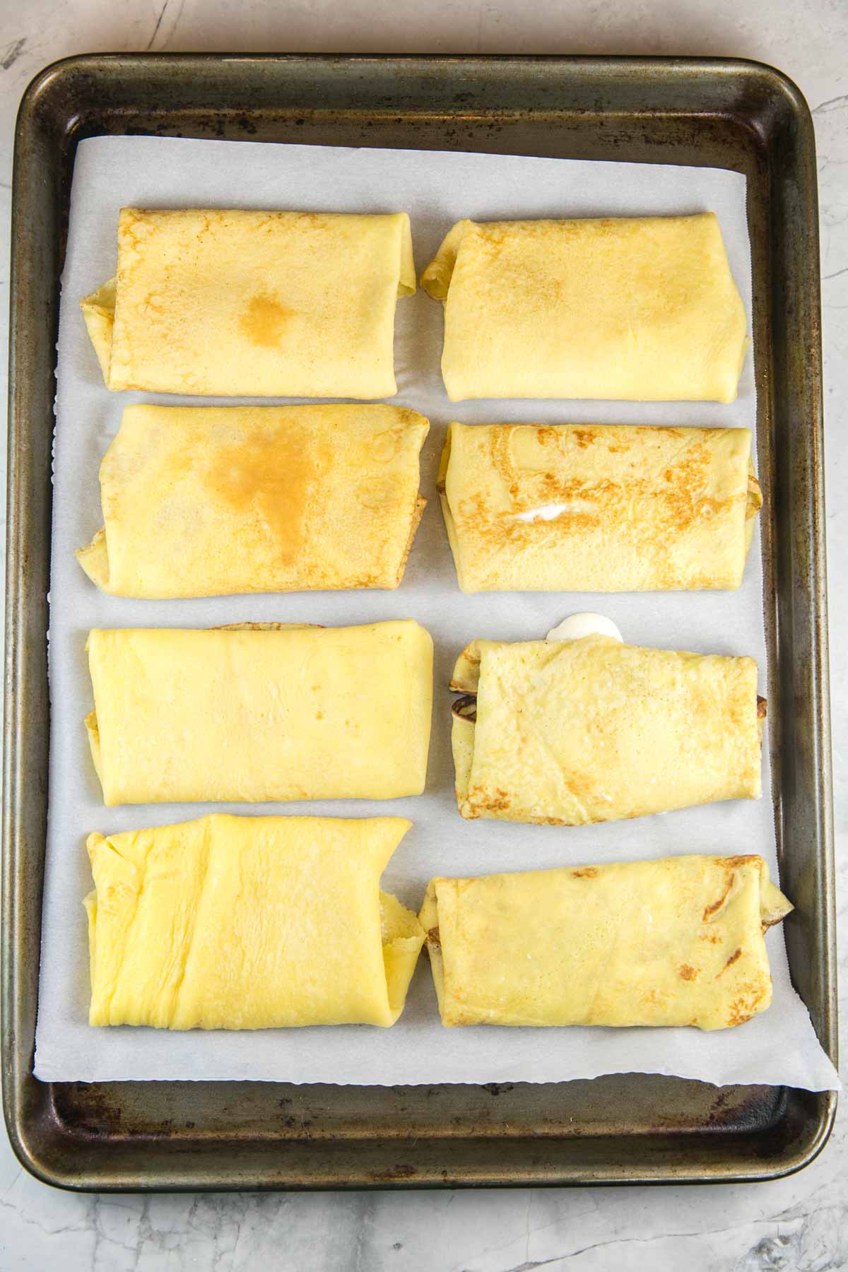 eight unbaked blintzes lined up on a cookie sheet