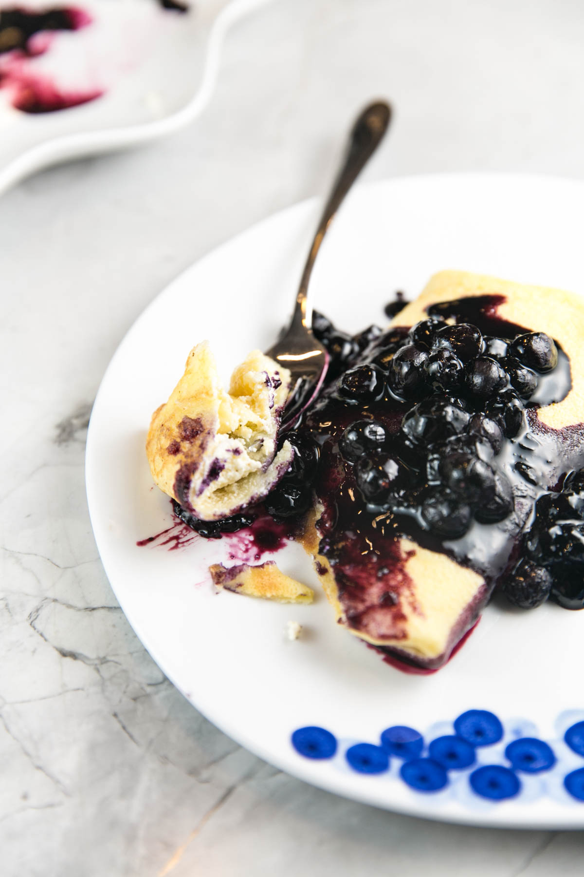 a ricotta filled blintz covered in blueberry sauce with a fork scooping up some of the filling