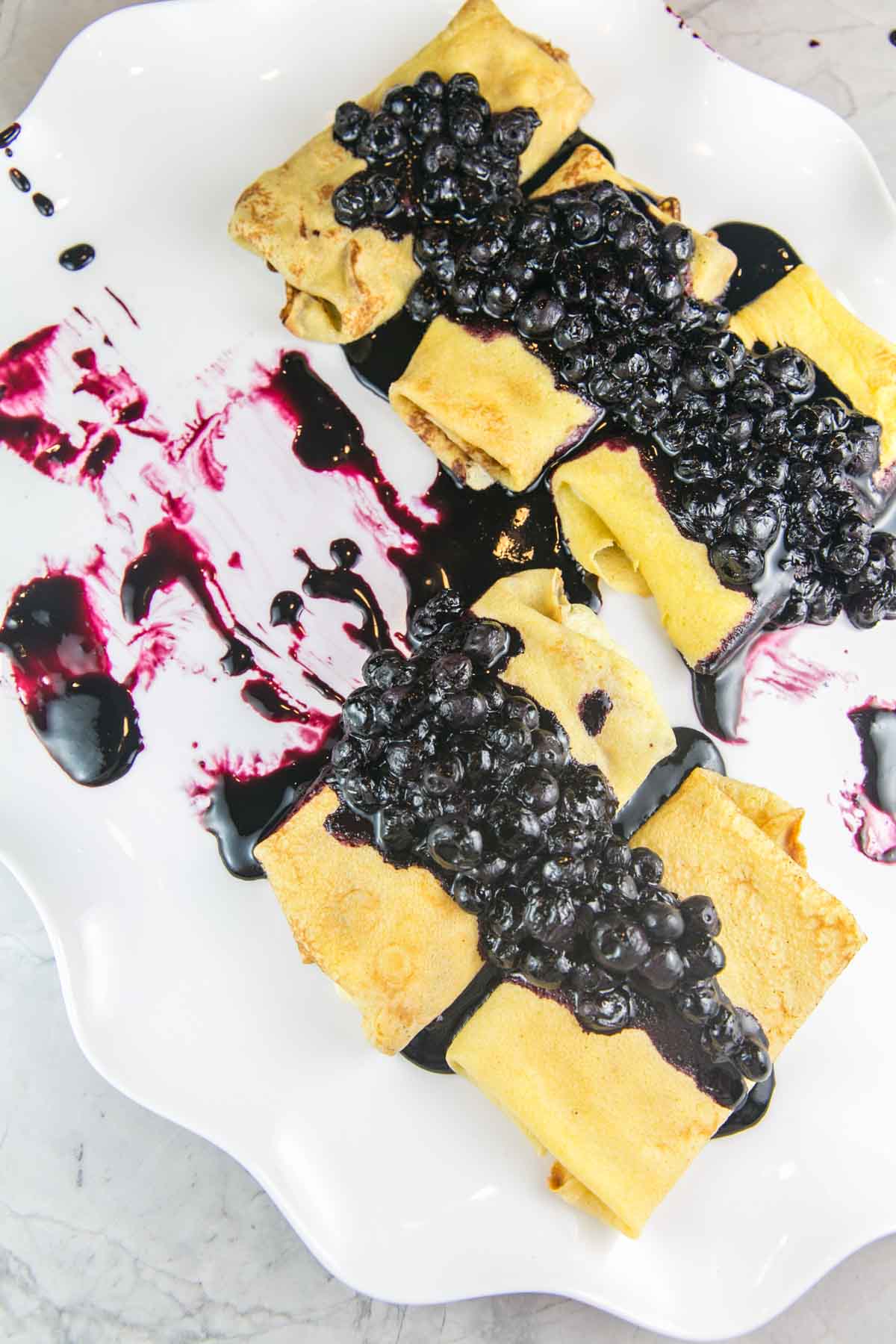five ricotta blintzes covered in blueberry sauce with sauce splattered across the plate