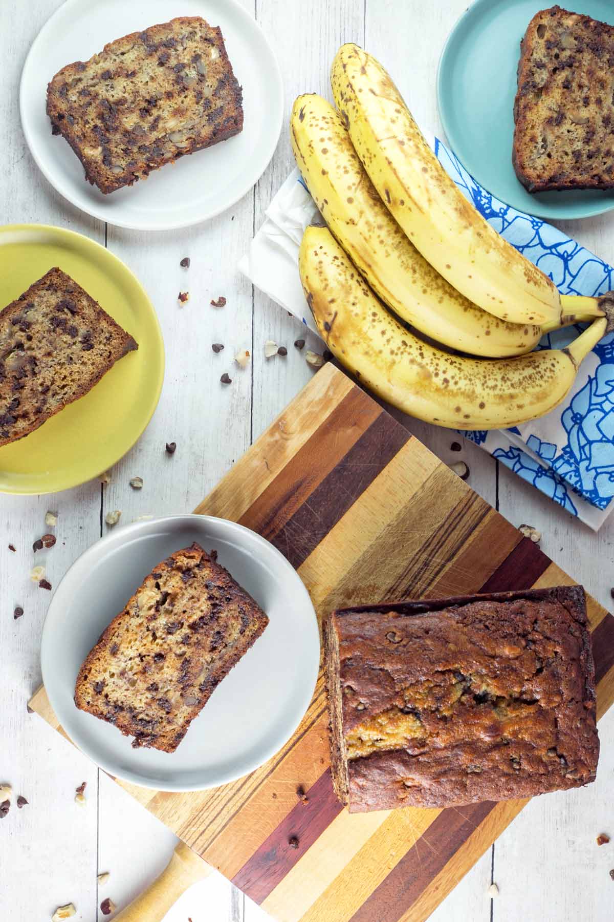 slices of banana bread on small dessert plates surrounded by bananas and hazelnuts