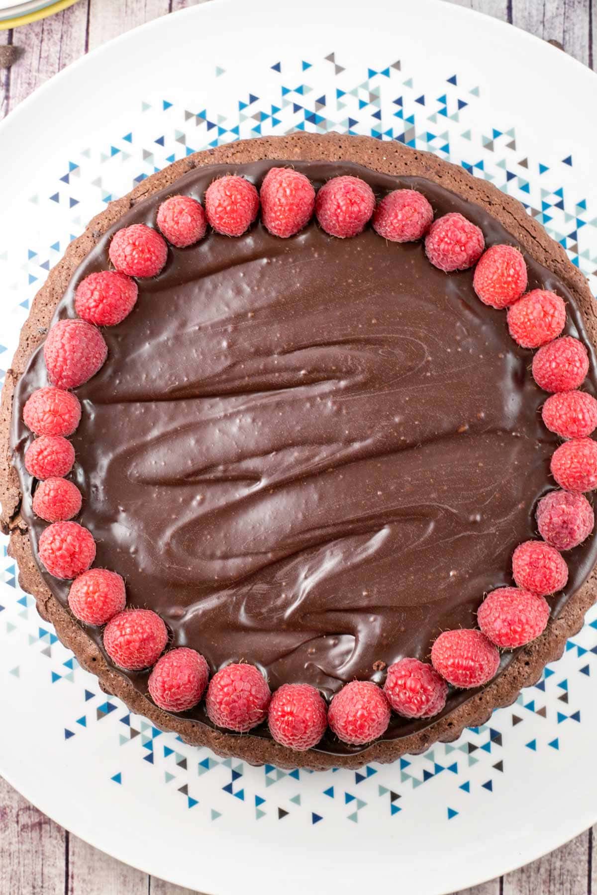 a flourless chocolate cake topped with chocolate ganache and a ring of raspberries