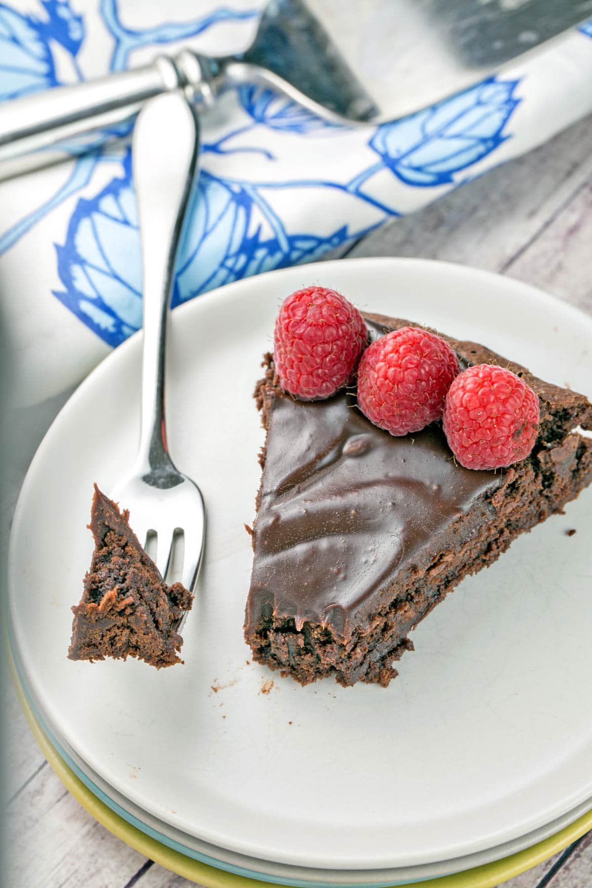 one slice of cake with chocolate ganache and three raspberries on a dessert plate